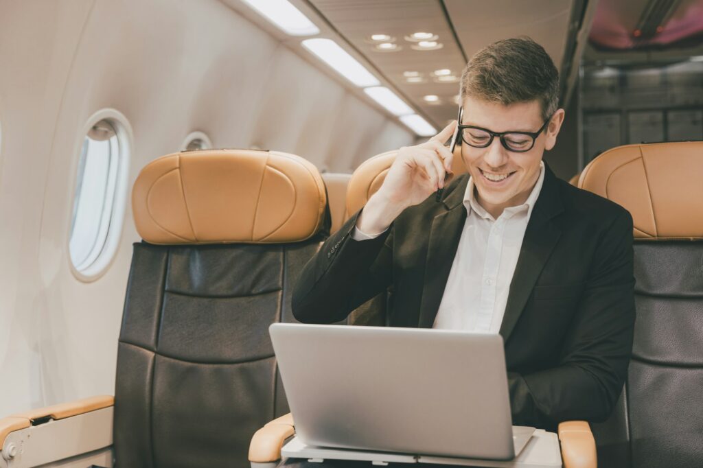 Businessman using satellite internet on laptop and phone calling business contact during air flight